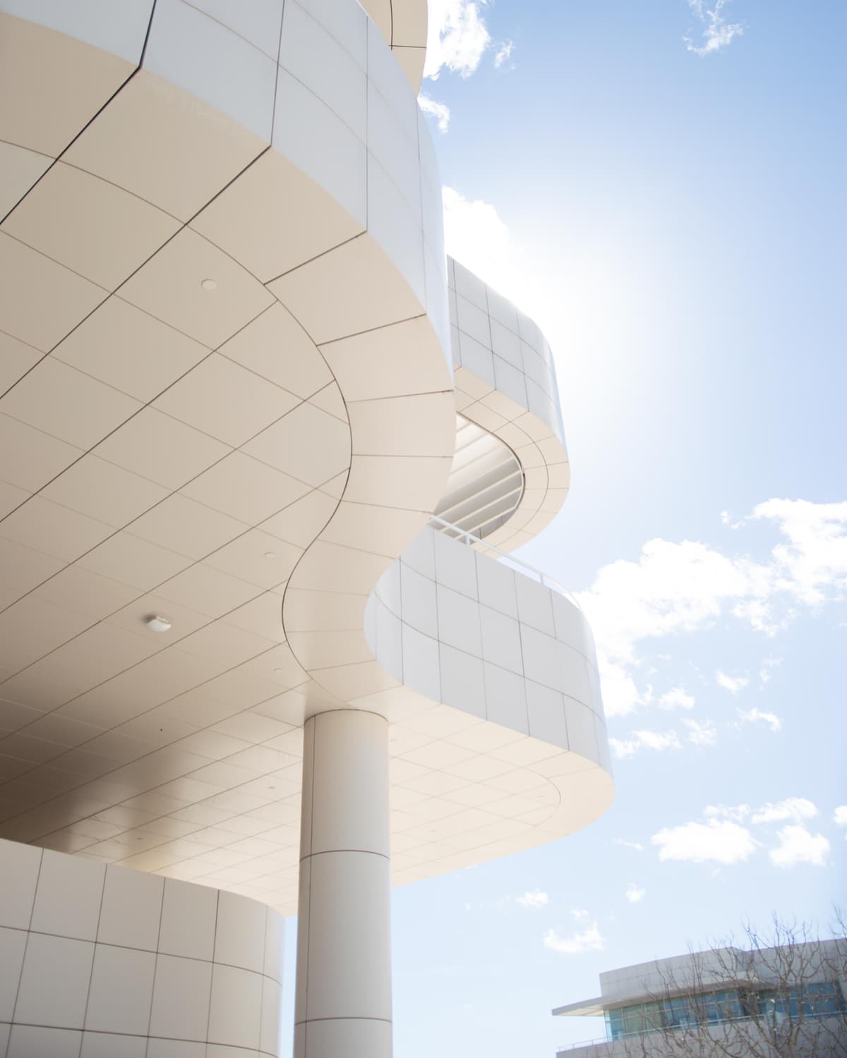 Looking up at the curved white travertine exterior of the Getty Center against a bright blue sky