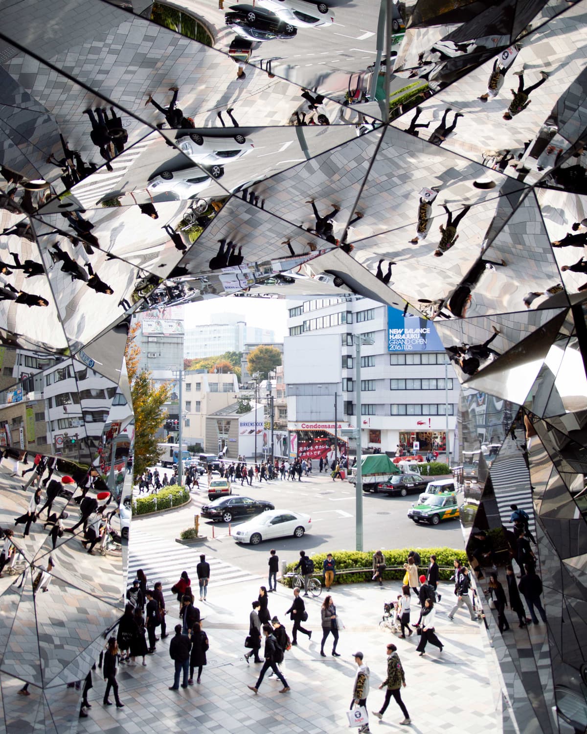A kaleidoscopic mirror art installation in Tokyo frames a busy street intersection below, multiplying reflections of pedestrians