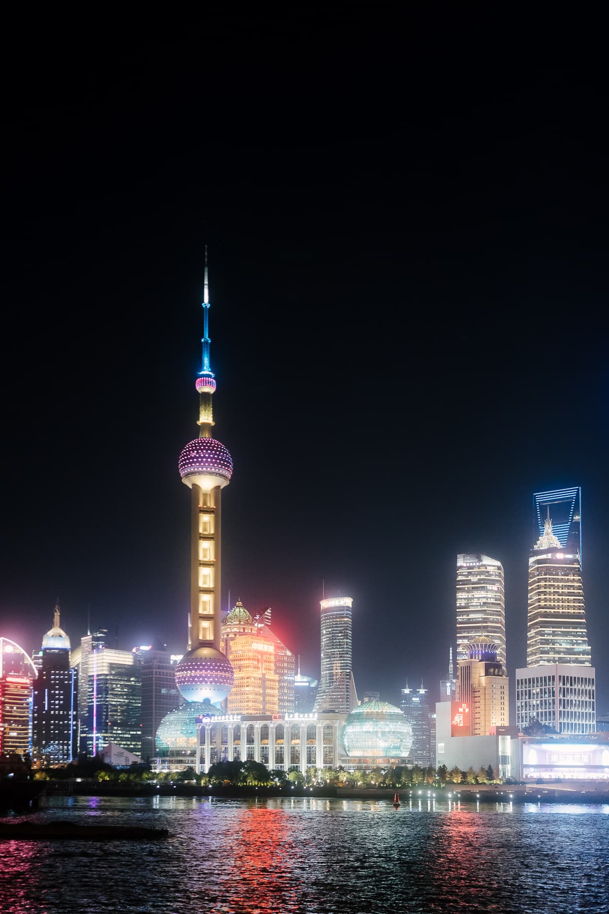 The illuminated Shanghai skyline at night, with the Oriental Pearl Tower reflected in the Huangpu River